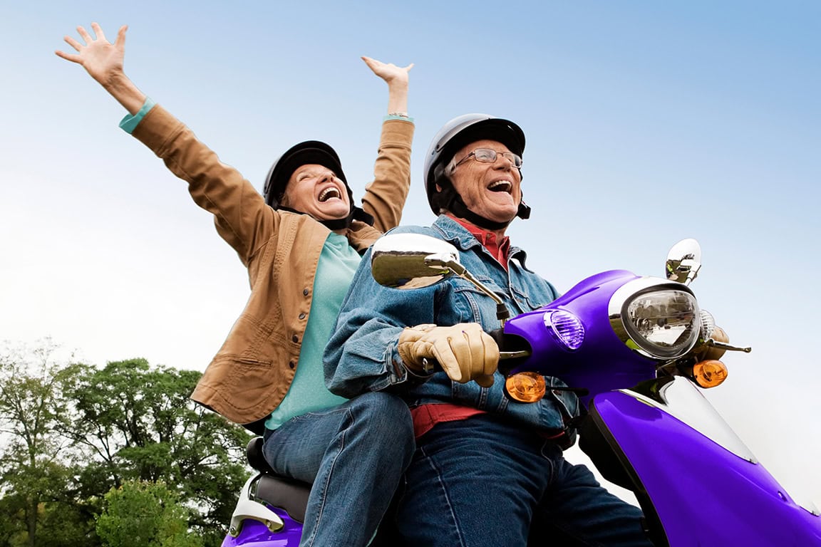 An elderly couple riding a scooter