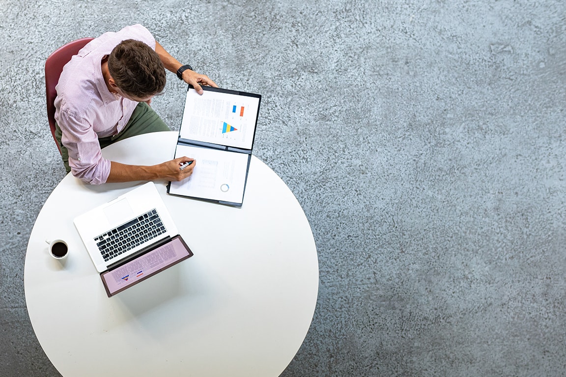 a man holding a report with a laptop on the table