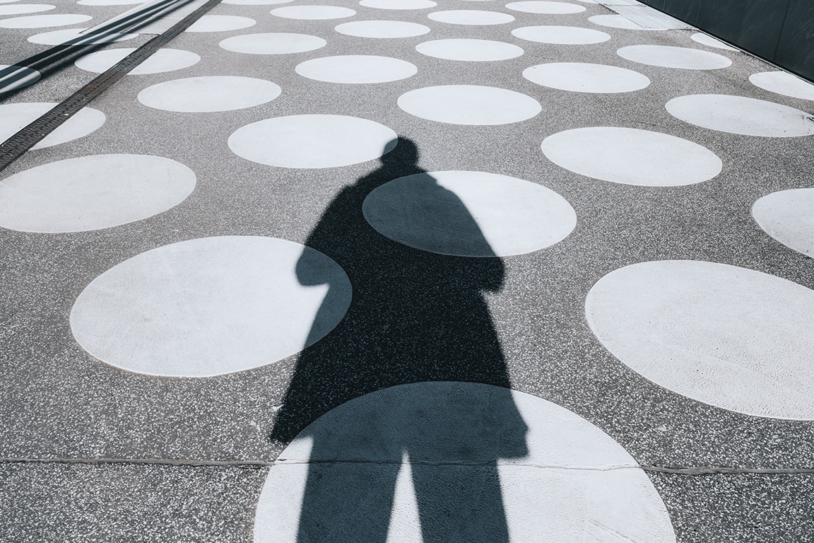 shadow of person standing on sidewalk that has geometric white circles