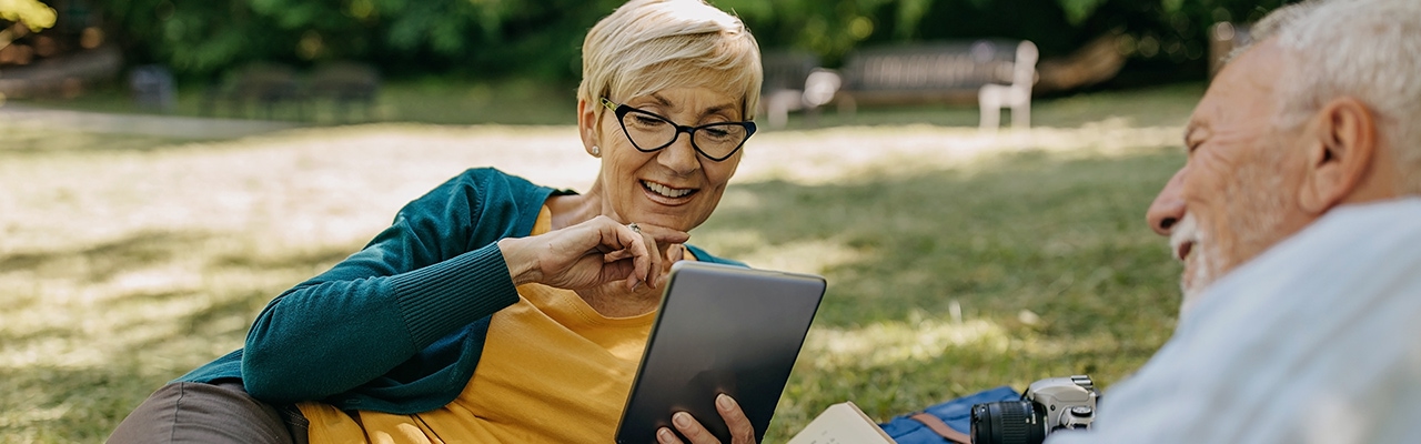 smiling man and women in a park reading from a tablet