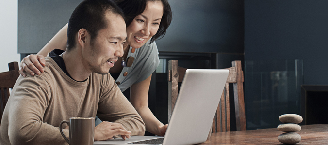Asian couple sitting down at table looking at laptop