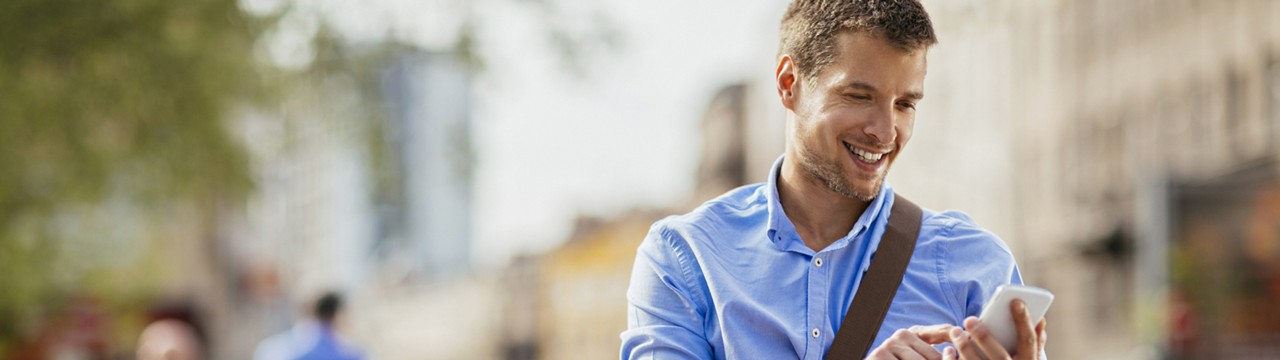 Smiling young man looking at cell phone with city scene in background.