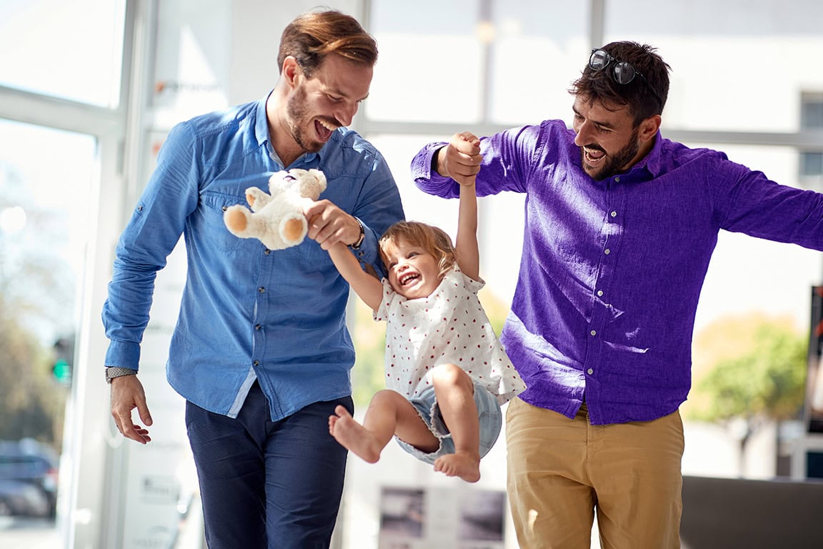 Two men holding up a child and toy bear